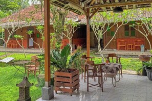 A covered outdoor area with wooden furniture, potted plants, and a tiled floor.