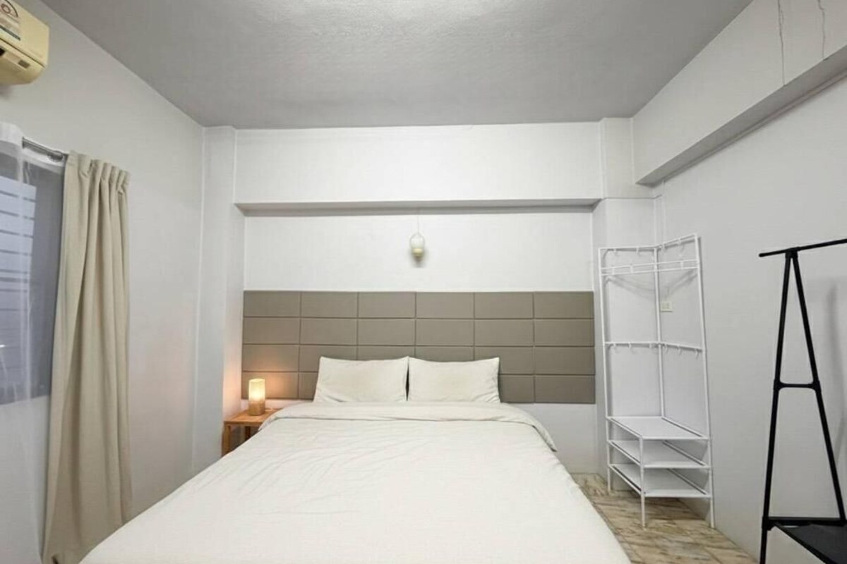 A hotel room with a bed, a nightstand, a wall-mounted shelf, and a wardrobe.