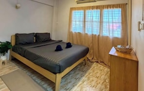 Una cama individual con cabecera, una mesita de noche, una planta pequeña en maceta y una ventana con cortinas.