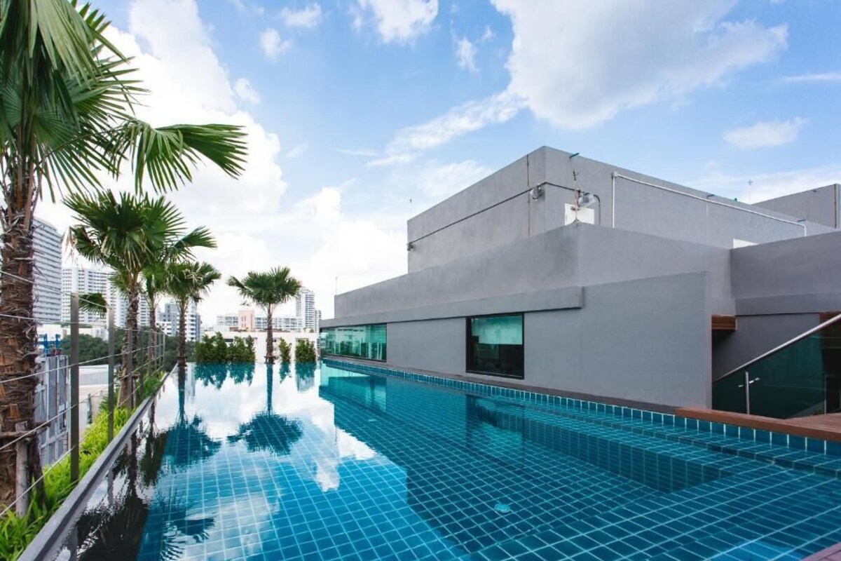 A modern building with a rooftop pool, surrounded by palm trees and cityscape.