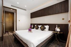 A modern hotel room with a large bed, dark wood headboard, and a small bedside table with a lamp. - High End Holiday Homes (Dubai)