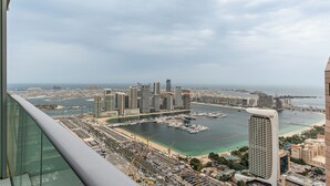 A high-rise hotel overlooking a marina with multiple boats, a beach, and a cityscape. - High End Holiday Homes (Dubai)