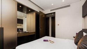 A modern hotel room with a large bed, a vanity with a mirror, and a walk-in closet. - High End Holiday Homes (Dubai)