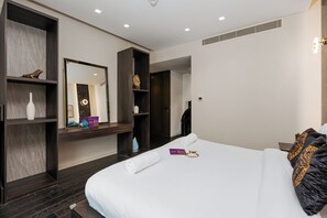 A modern hotel room with a large bed, dark wood shelving, a mirror, and a small table with toiletries. - High End Holiday Homes (Dubai)