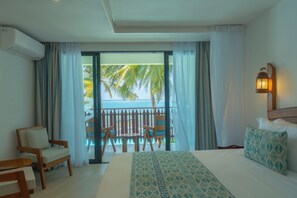 A hotel room with a bed, a chair, a small table, a balcony with a view of the sea and palm trees, and an air conditioning unit.