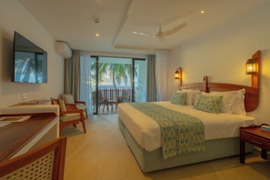 A hotel room with a bed, desk, chairs, a TV, a balcony with a view, and a ceiling fan. - Heritage Hotels Ltd (Mombasa)