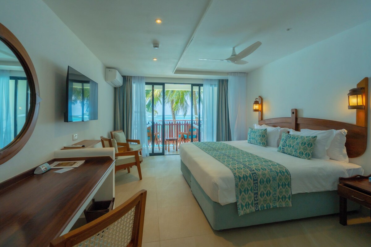 A hotel room with a bed, desk, chairs, a TV, and a balcony with a view.