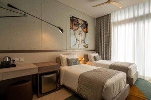 Ein Hotelzimmer mit zwei Betten, einem Schreibtisch, einer Kaffeemaschine, einer Wandlampe und einem Gemälde.