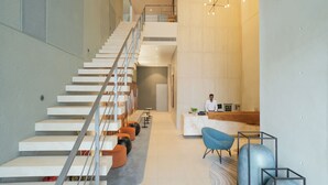 A modern interior with a staircase, seating area, reception desk, and a person standing near the desk. - Sesaya Poshtel & Bistro (Sri Jayawardenepura Kotte)