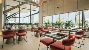 A modern dining area with tables and chairs, large windows, and a view of the cityscape. - Sesaya Poshtel & Bistro (Sri Jayawardenepura Kotte)