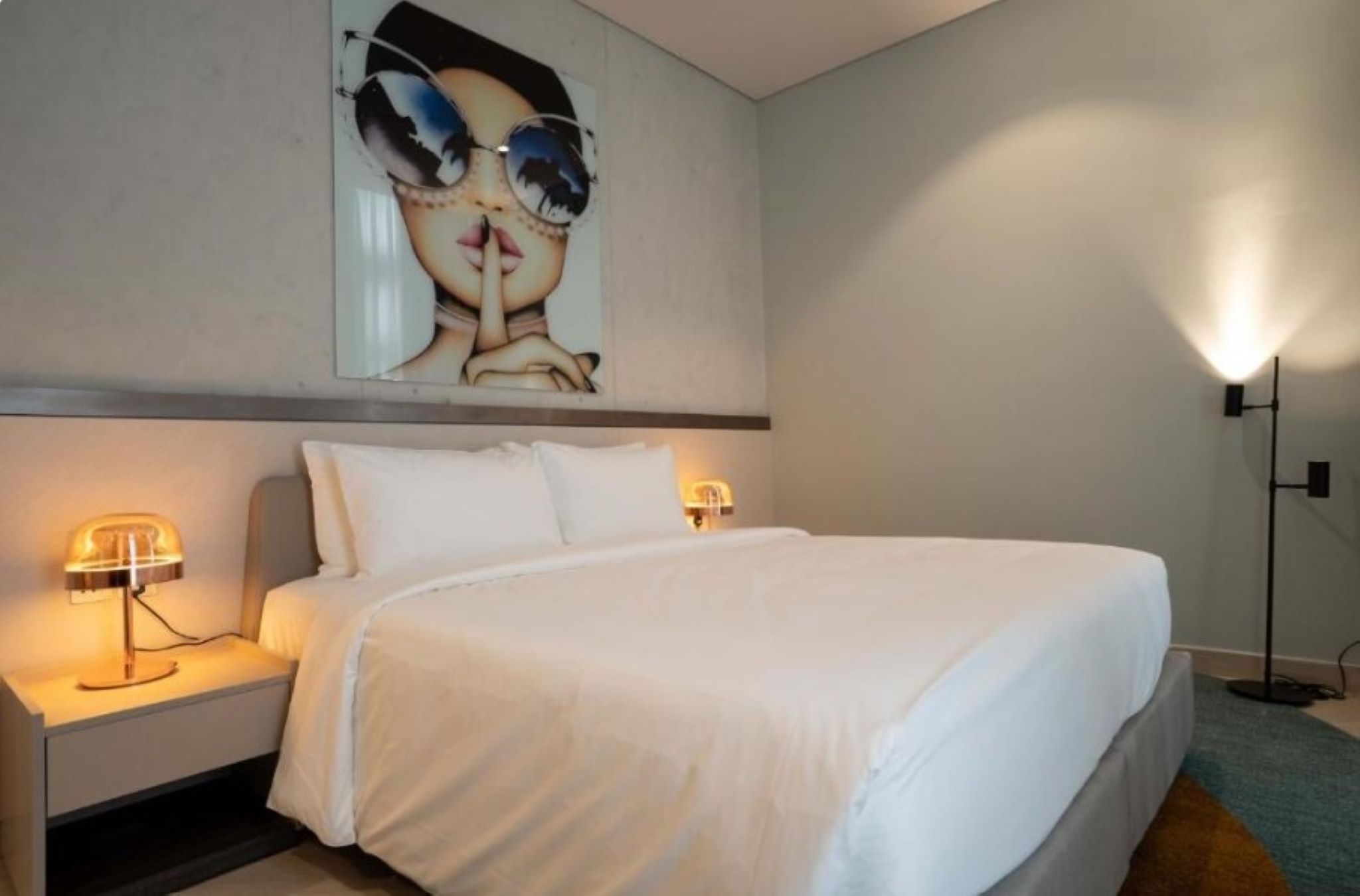 A hotel room with a large bed, two bedside lamps, a wall-mounted artwork, and a floor lamp.