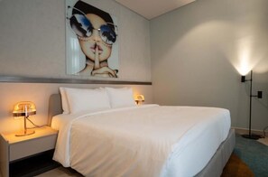 Ein Hotelzimmer mit einem großen Bett, zwei Nachttischlampen, einem Wandbild und einer Stehlampe.