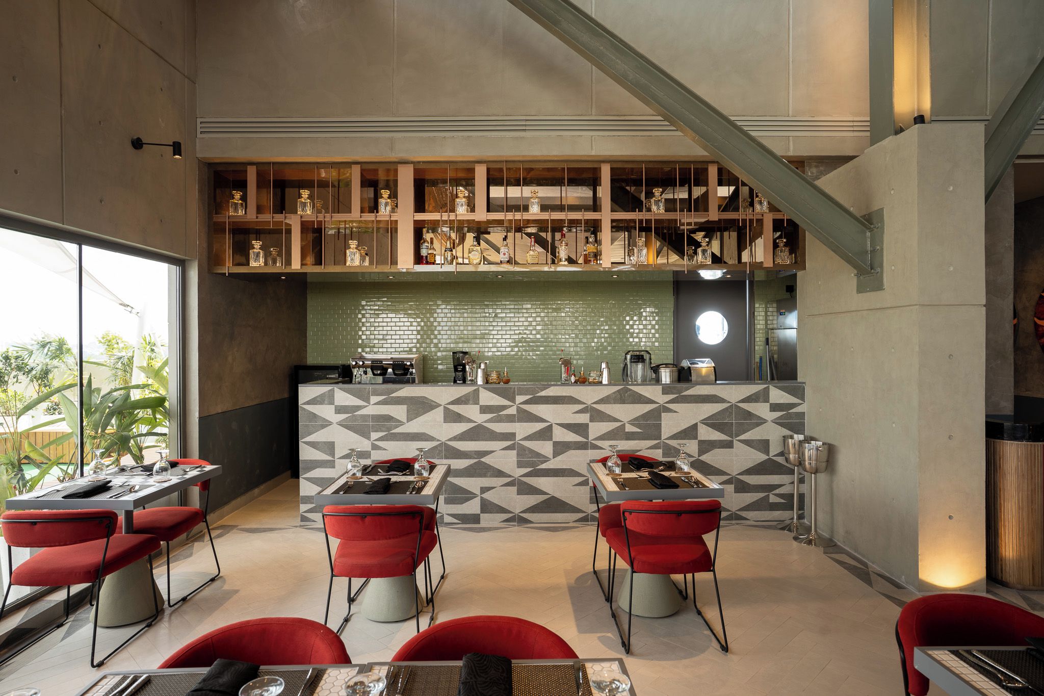 A modern restaurant with a geometric tile backsplash, red chairs, and a bar area with shelves of bottles.