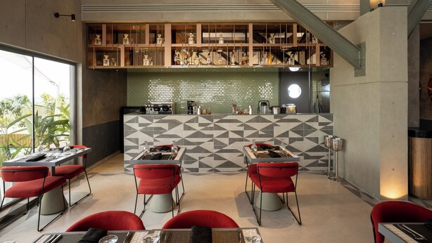 Un restaurante moderno con un salpicadero de azulejos geométricos, sillas rojas y una zona de bar con estantes llenos de botellas.