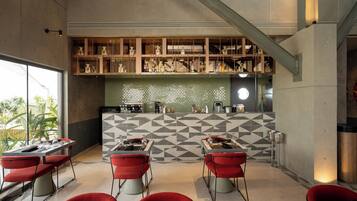 A modern restaurant with a geometric tile backsplash, red chairs, and a bar area with shelves of bottles.