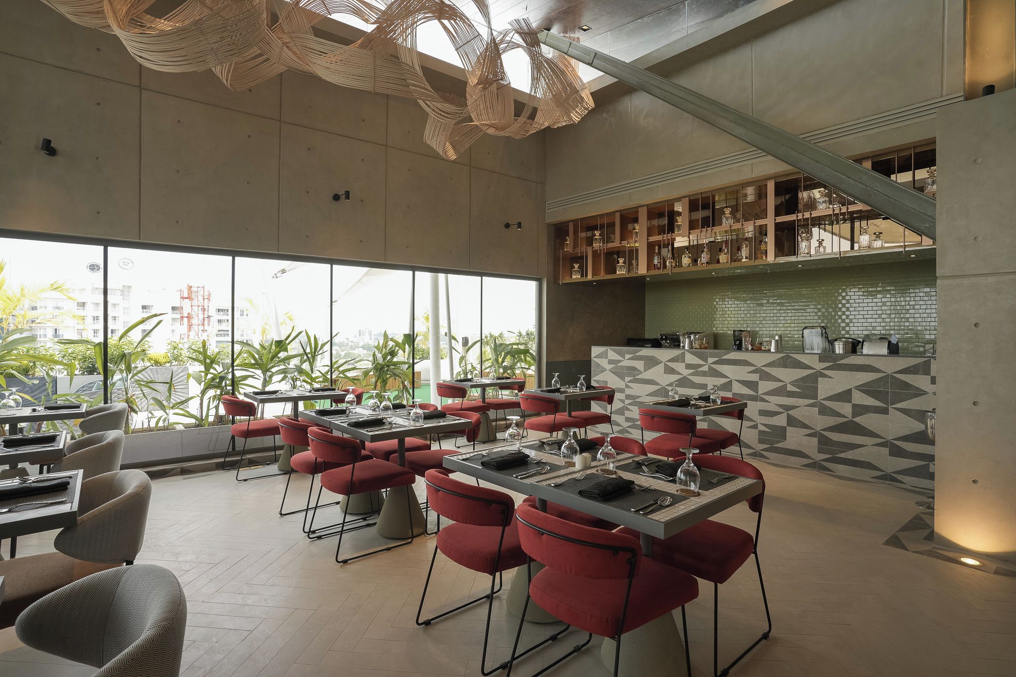 A modern restaurant with red chairs and tables, large windows, and a geometric tile backsplash.