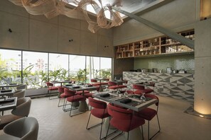 Un restaurante moderno con sillas y mesas rojas, ventanas amplias y un backsplash de azulejos geométricos.
