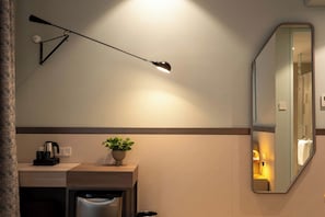 A hotel room with a desk, a mirror, a ceiling lamp, a potted plant, and a trash bin. - Sesaya Poshtel & Bistro (Sri Jayawardenepura Kotte)