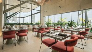 Un comedor moderno con mesas y sillas, ventanas amplias y vistas a la ciudad.