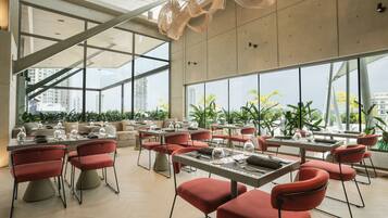 A modern dining area with tables and chairs, large windows, and a view of the cityscape.