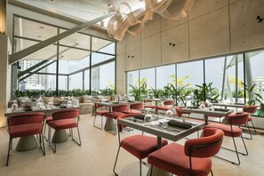 Un comedor moderno con mesas y sillas, ventanas amplias y vistas a la ciudad.