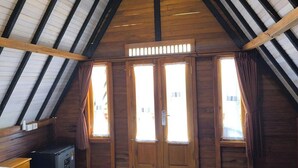Una stanza con soffitto in legno spiovente, un letto, una piccola scrivania e due finestre con tende.