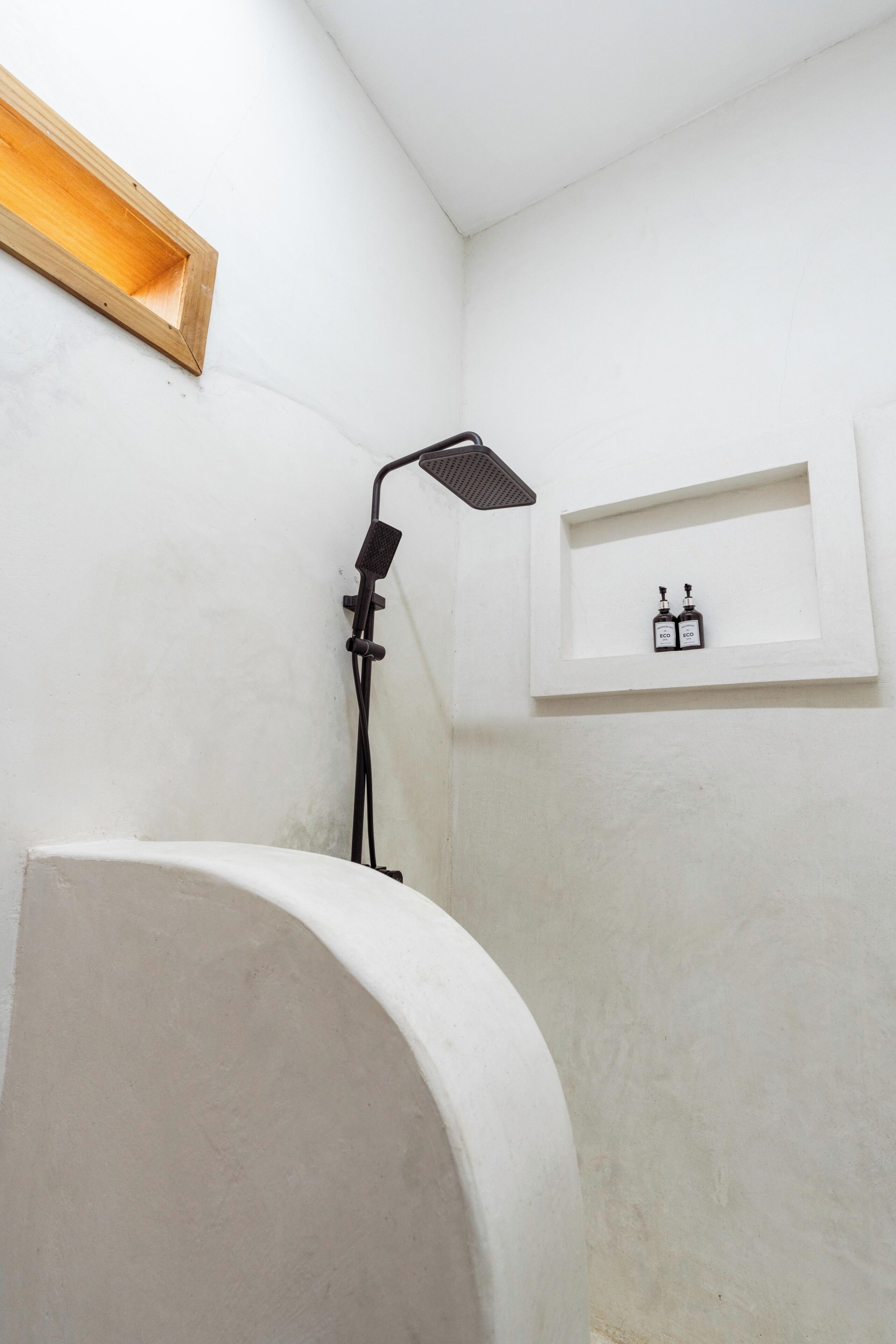 Un baño con ducha, un lavabo blanco y una repisa con dos botellas.