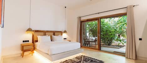Une chambre à coucher avec un lit, des lampes de chevet, un ventilateur de plafond, une grande fenêtre avec des rideaux et une vue sur la verdure à l’extérieur.