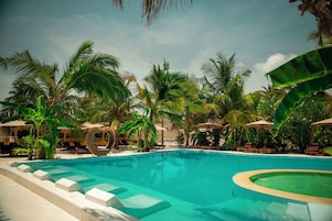A swimming pool with lounge chairs and umbrellas, surrounded by palm trees.