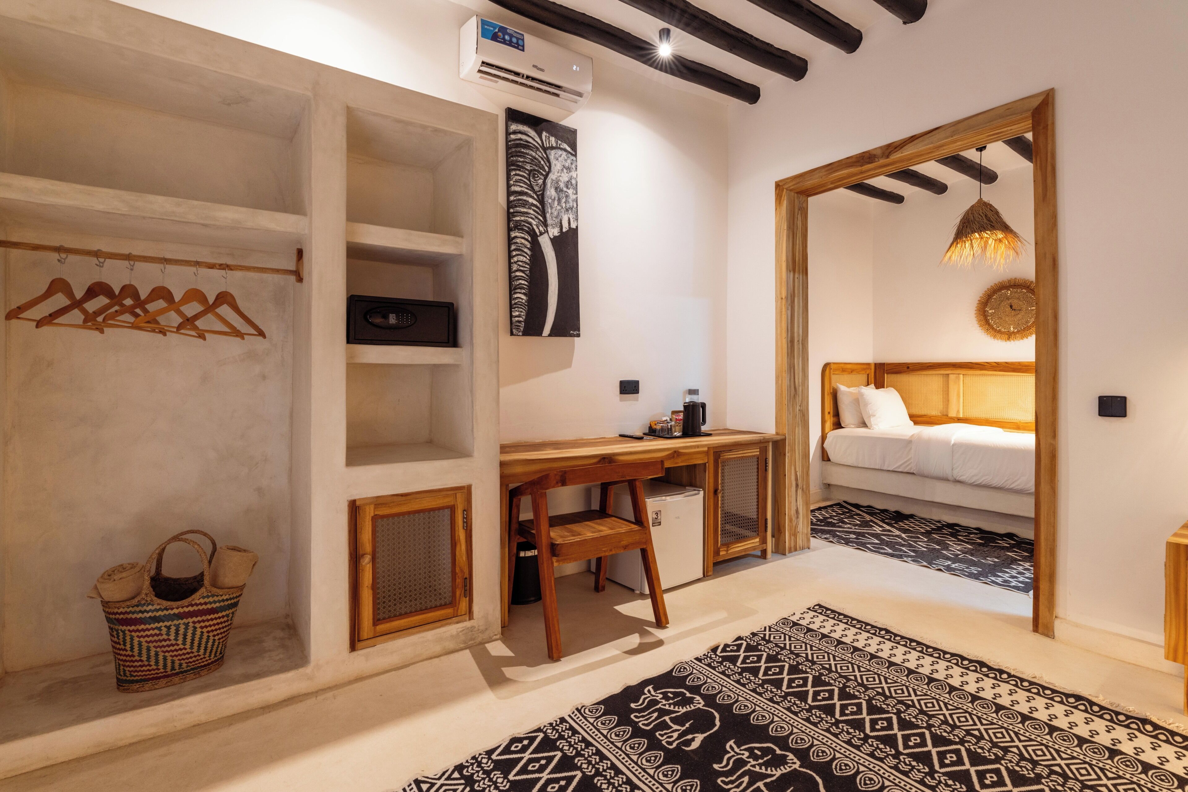 A compact room with a bed, a desk, a wardrobe, and a hanging coat rack.