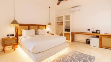 A bedroom with a bed, bedside tables, a ceiling fan, an air conditioning unit, a desk, and a trash bin.