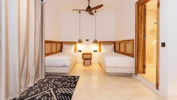 Una habitación con dos camas, ventilador de techo, luces fijadas en la pared, una mesita y una puerta.