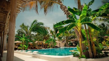 Un área de piscina con una piscina azul cristalina, rodeada de palmeras y tumbonas.