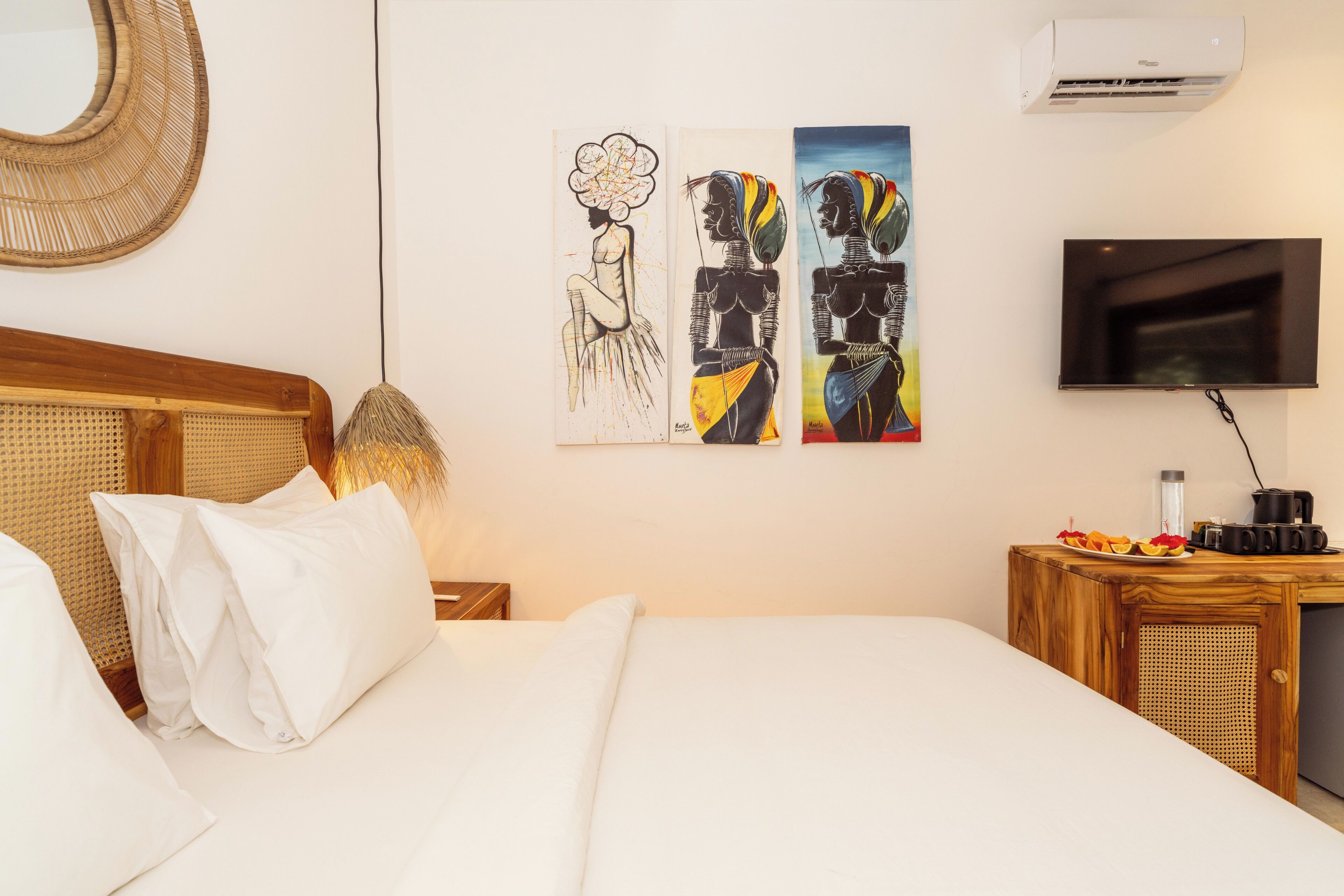 A hotel room with a bed, a television, and artwork on the wall.