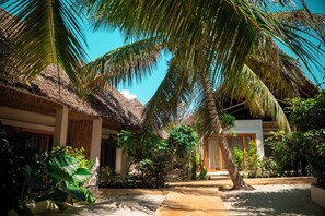 A tropical resort with thatched-roof buildings, lush greenery, and a clear blue sky. - LUJO Zanzibar Resort (Paje)