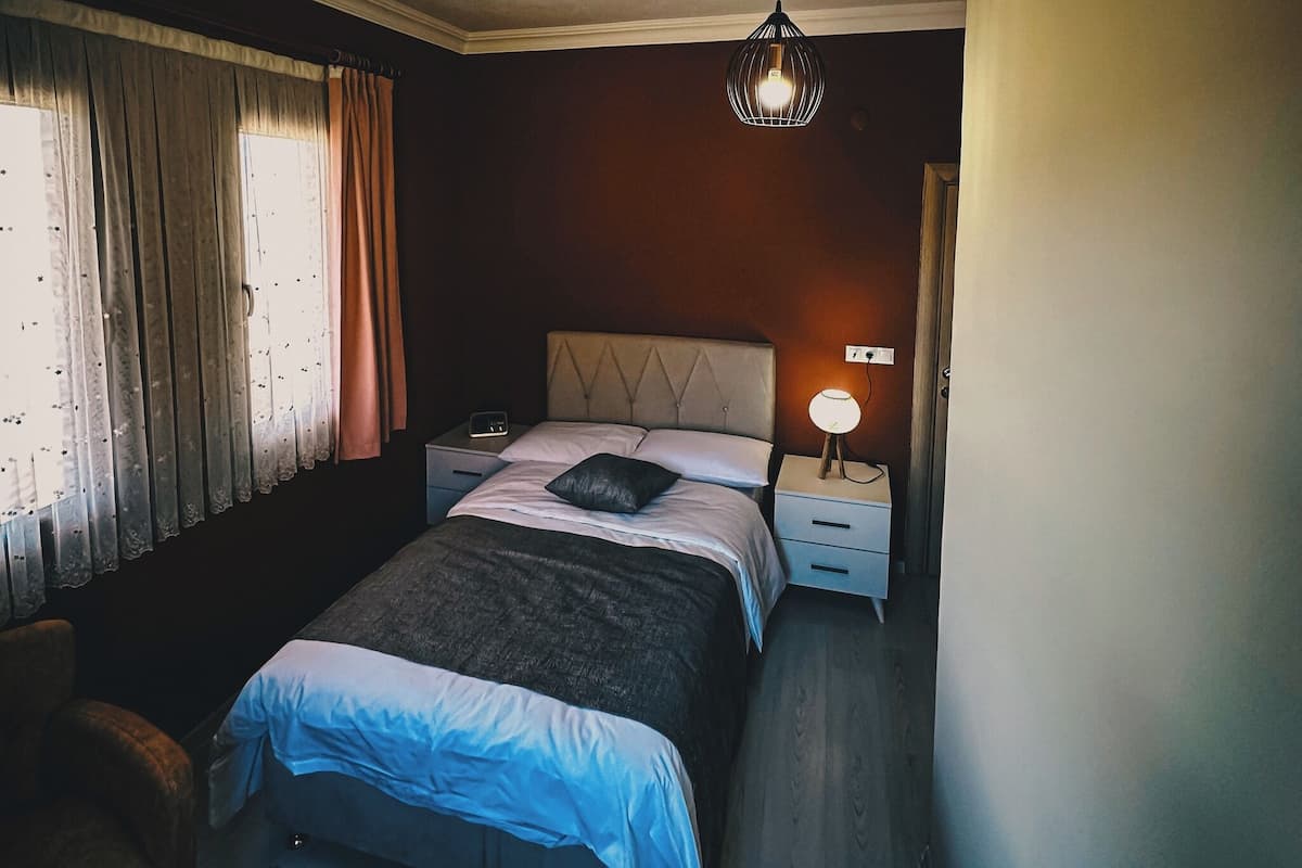 Ein Schlafzimmer mit einem Bett, Nachttischen, einer Pendelleuchte und einem Fenster mit Vorhängen.