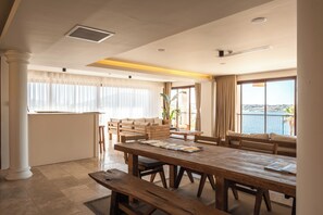 A spacious dining area with a large wooden table, benches, and a view of the water. - L'saranda House Cesme (Çeşme)