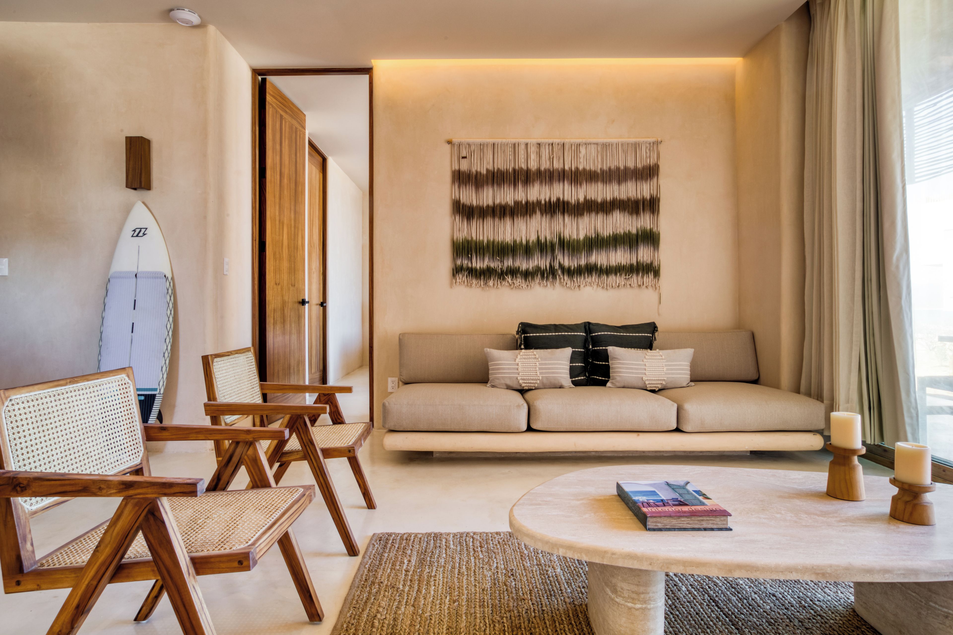 Una sala de estar con sofá, sillas, una tabla de surf y un tapiz en la pared.