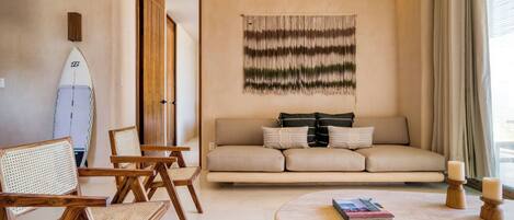 A living room with a sofa, chairs, a surfboard, and a wall hanging.
