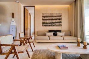 A living room with a sofa, chairs, a surfboard, and a wall hanging. - Amina Wind Resort (La Ventana)