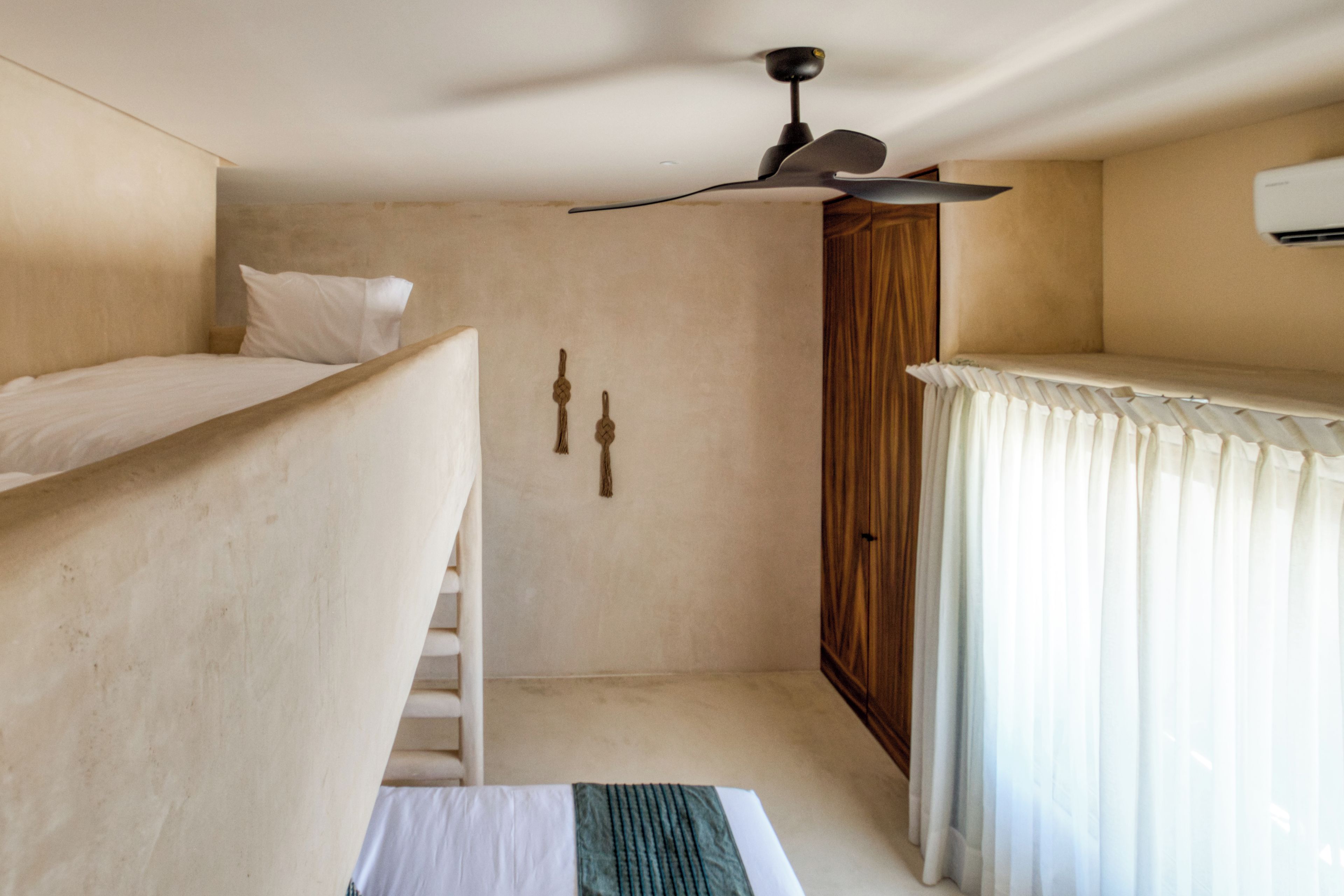 Una habitación pequeña con literas, ventilador de techo, armario y ventana con cortinas.