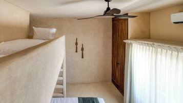 A compact room with a bunk bed, a ceiling fan, a wardrobe, and a window with curtains.