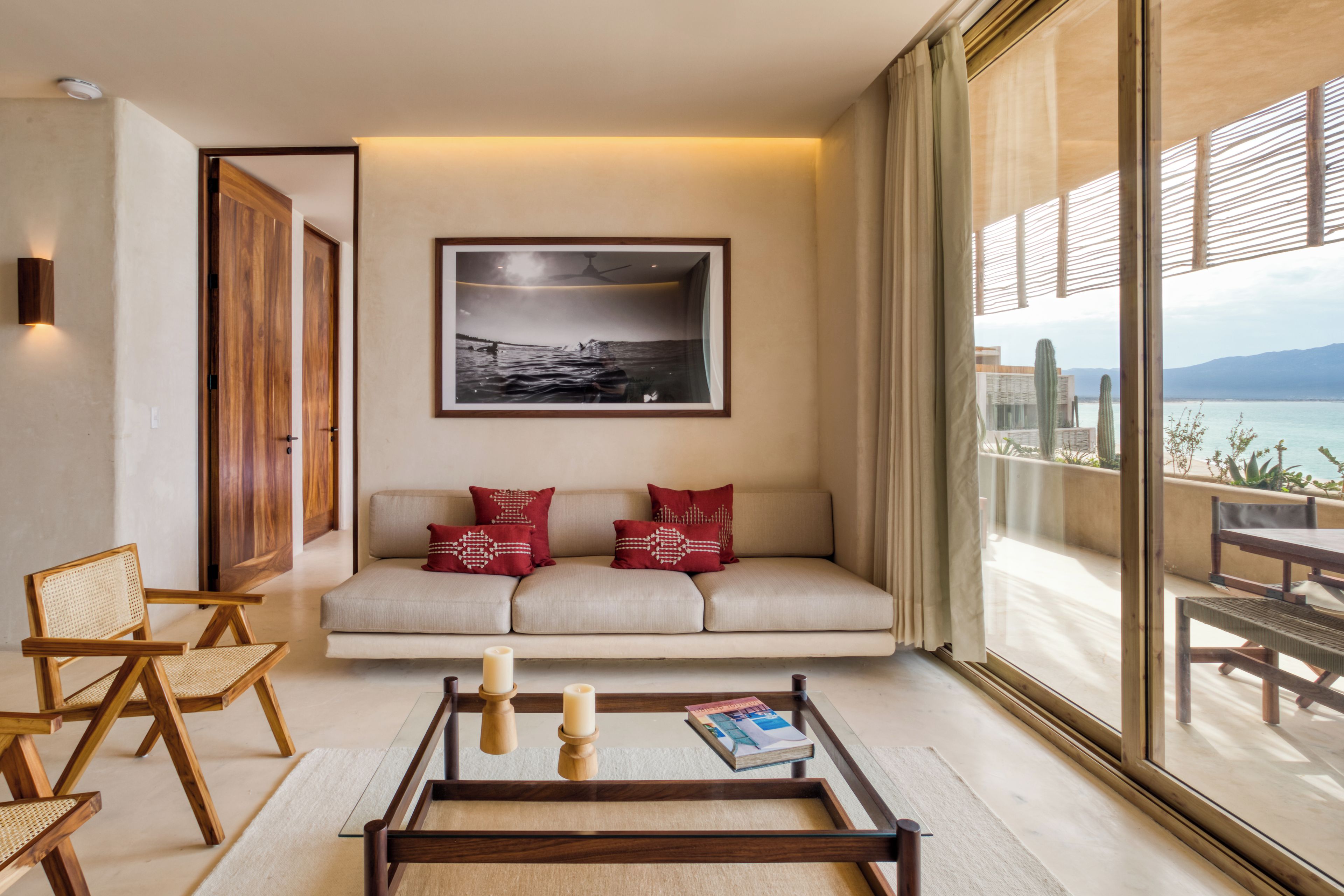 A modern living room with a sofa, two red pillows, a coffee table with candles, and a framed picture on the wall.