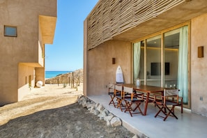 Un edificio moderno con un comedor que presenta una mesa y sillas de madera, un amplio ventanal y vistas a la playa.