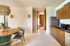 A modern kitchen with wooden cabinets, a stainless steel refrigerator, and a dining area with a round table and chairs. - Amina Wind Resort (La Ventana)