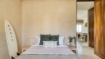 A bedroom with a bed, pillows, a surfboard, and a wooden door.