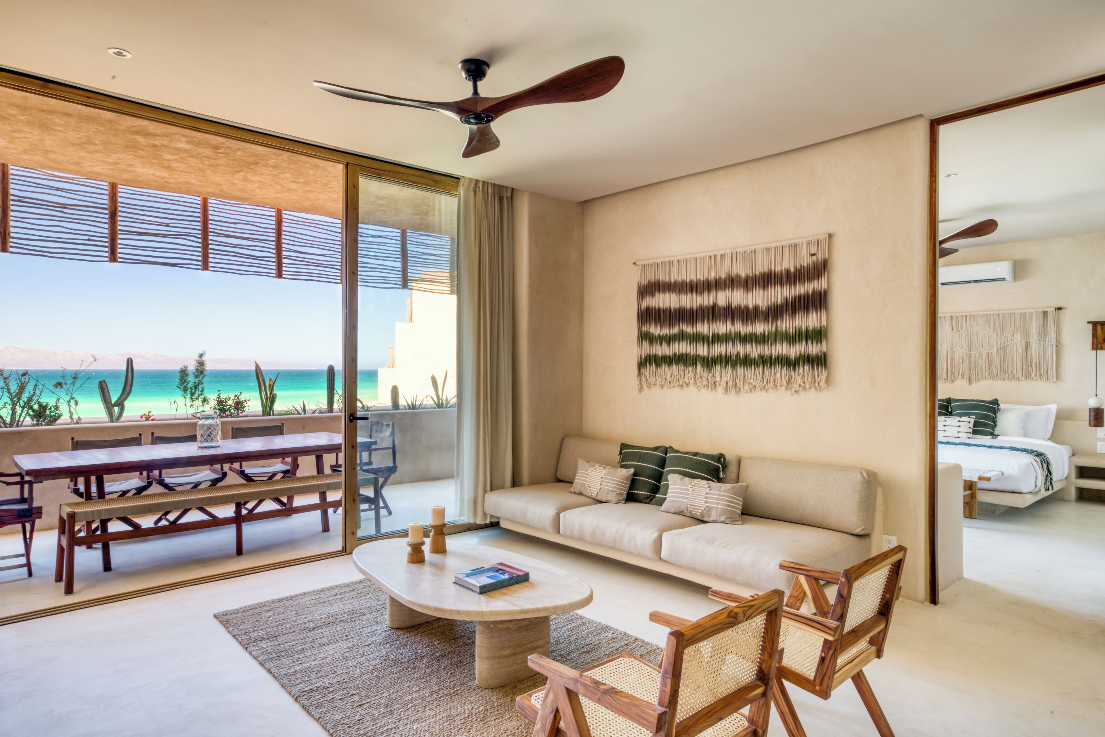 A modern living room with a large window, a ceiling fan, a sofa, a coffee table, and a dining area with benches.