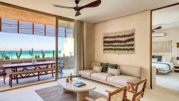 A modern living room with a large window, a ceiling fan, a sofa, a coffee table, and a dining area with benches.