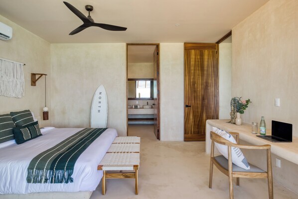 Un dormitorio con cama, escritorio, silla, una tabla de surf y ventilador de techo.