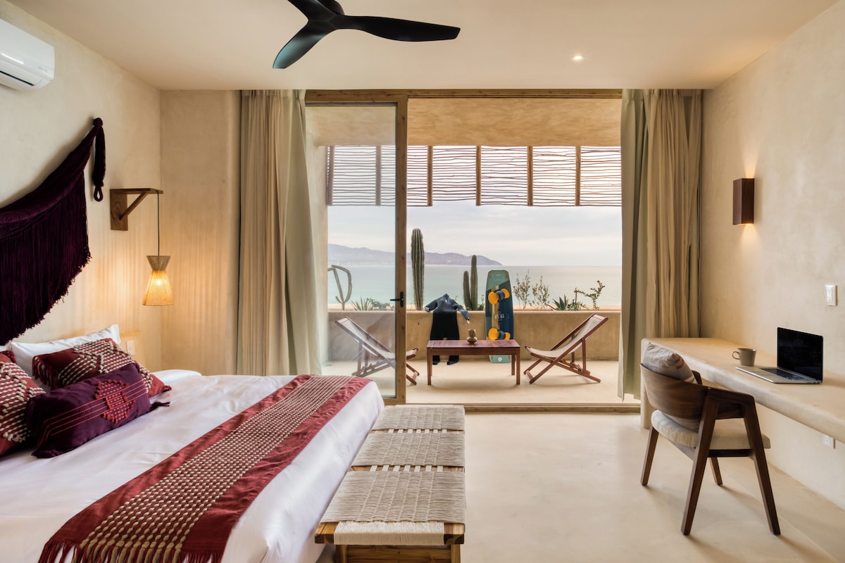 Habitación de hotel con cama, escritorio, una computadora portátil y vista al mar.